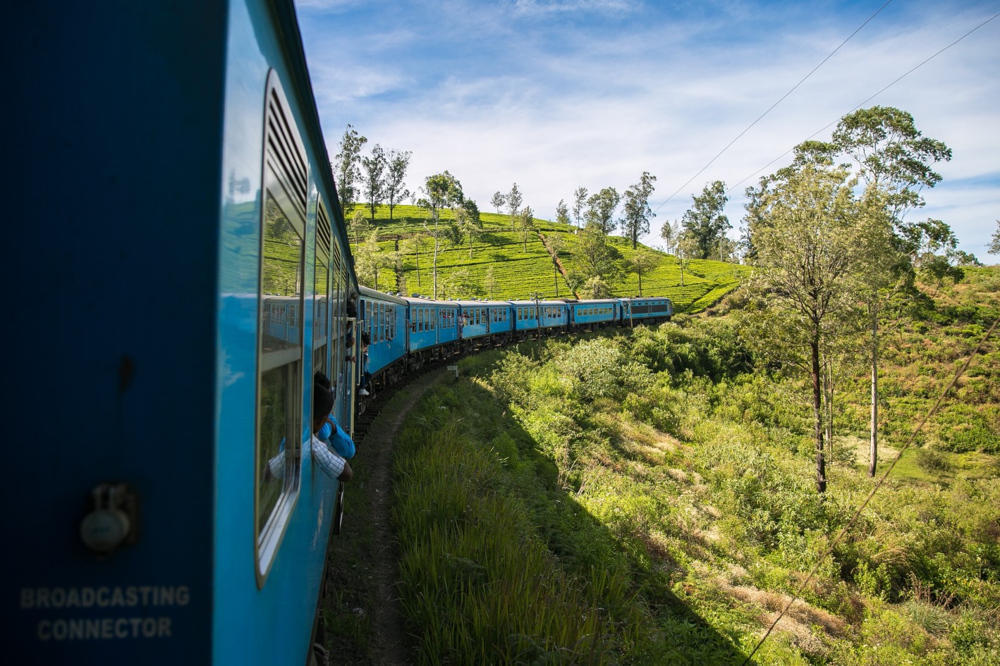 A blue train crossing the Nine Arches Bridge at sunrise through Sri Lanka's tea country